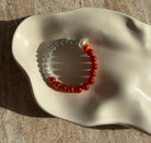 Nahaufnahme eines handgefertigten Armbands mit grauen und orangen Perlen, mittig verziert mit einer weißen und einer bernsteinfarbenen Kugel.